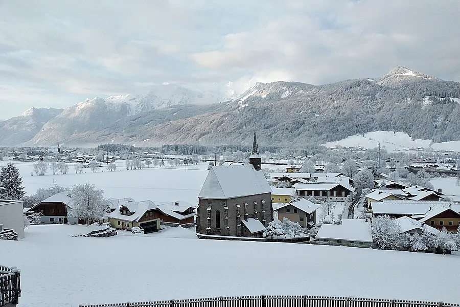 im Vordergrund verschneite Wiese vor unserem Haus, dann Kirche Sankt Margarethen mit Blick zum Rossfeld und Göll